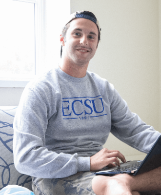 ECSU student smiling at the camera while they are working on laptop.