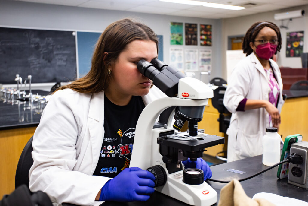 Student examines a specimen under a microscope during a biology lab session.