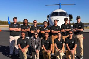 Group of ECSU Aviation students pose on an airport ramp in front of a private jet while wearing matching ECSU Aviation polo shirts.