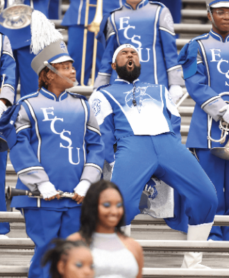 ECSU band member shouting from the stands surrounding by other band members in uniform