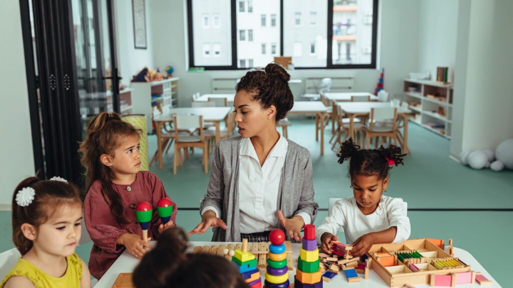 A teacher with curly hair is educating children with wooden building blocks.