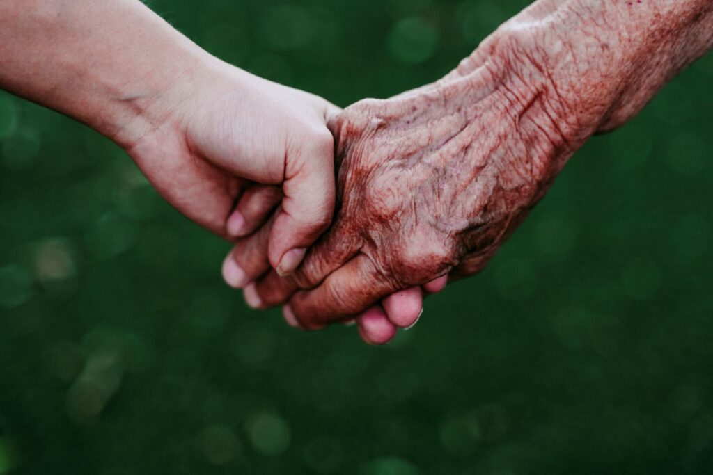 An extreme close-up captures the touching of hands between a young adult and a senior, conveying connection and caring.