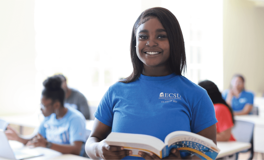 Student smiling at camera holding an open textbook
