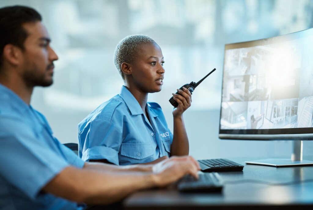 Two security professionals are at work monitoring surveillance systems. 