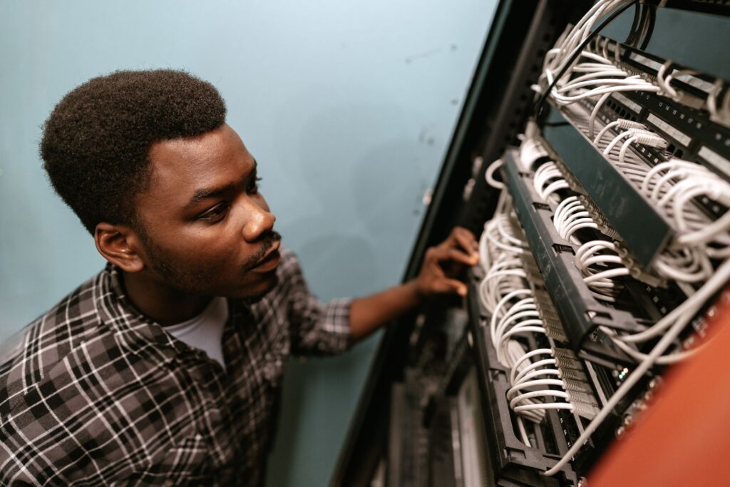 A young adult man in a plaid shirt is shown inspecting a server rack.