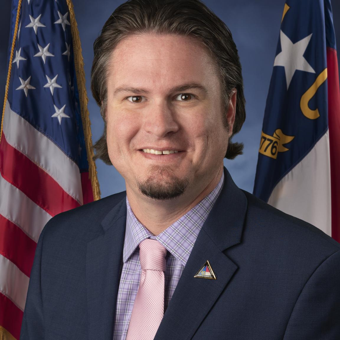 Head shot of Justin Graney with American and North Carolina flags behind him