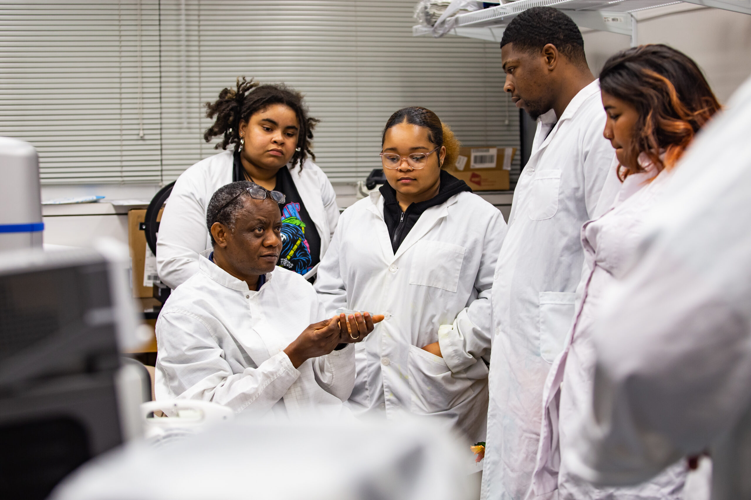 ECSU students gathered around their instructor for a lesson, all wearing lab coats.