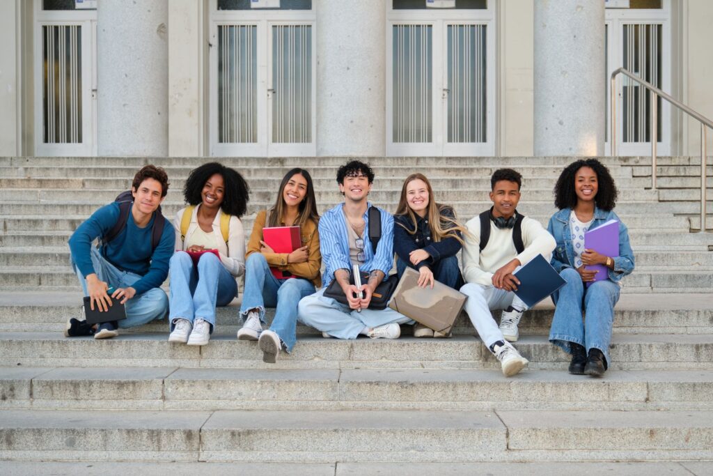 A group of six young adults sits on the wide steps of a building.