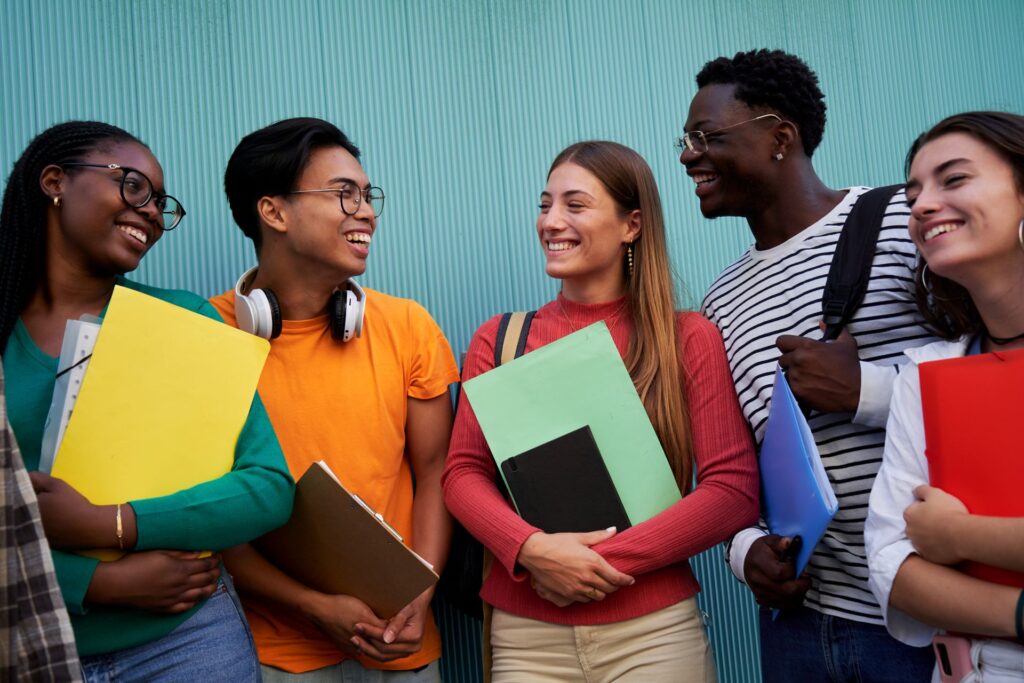Five young adults are visible in this lighthearted, daytime shot, carrying books and notebooks.