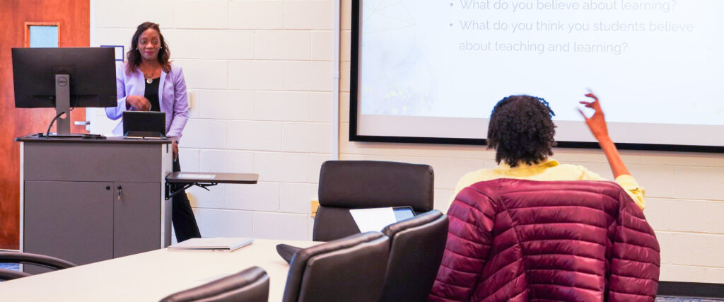 Center of Teaching, Learning and Digital Education staff hosting a workshop. An attendee is sitting down and raising their hand for a comment or question.