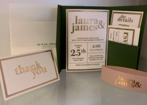 Wedding stationery collection featuring an invitation, RSVP card, details card, envelope, place card, and thank-you card. The design uses metallic gold typography, soft neutral tones, and coordinated print materials displayed as a complete wedding suite.