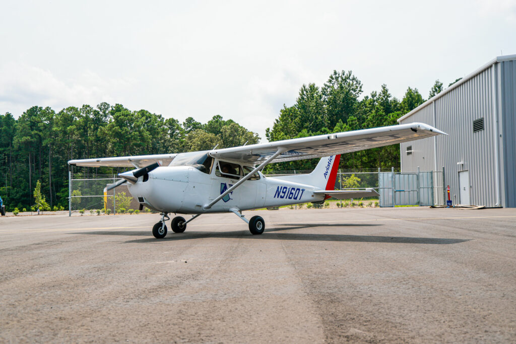 ECSU Aviation training aircraft parked on an airport tarmac near a hangar. The single-engine airplane displays Elizabeth City State University aviation branding and registration number N916QT, with trees and airport facilities visible in the background.